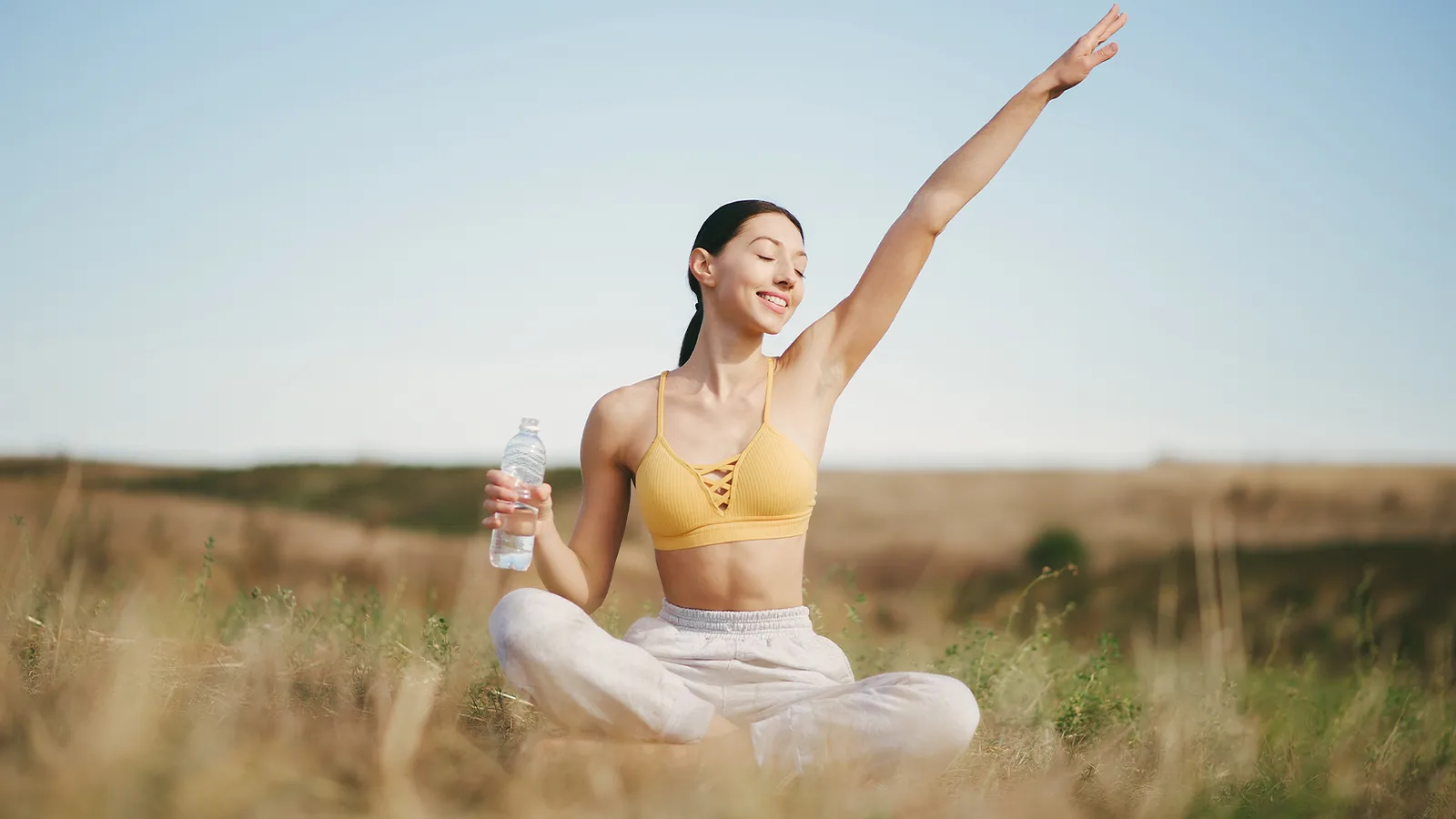 Woman sitting outdoors with one arm raised and her eyes closed