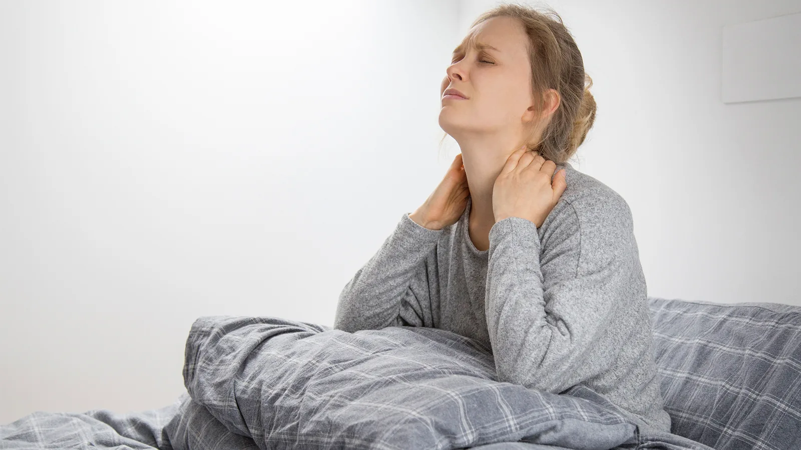 Woman sitting up in bed holding the side of her neck