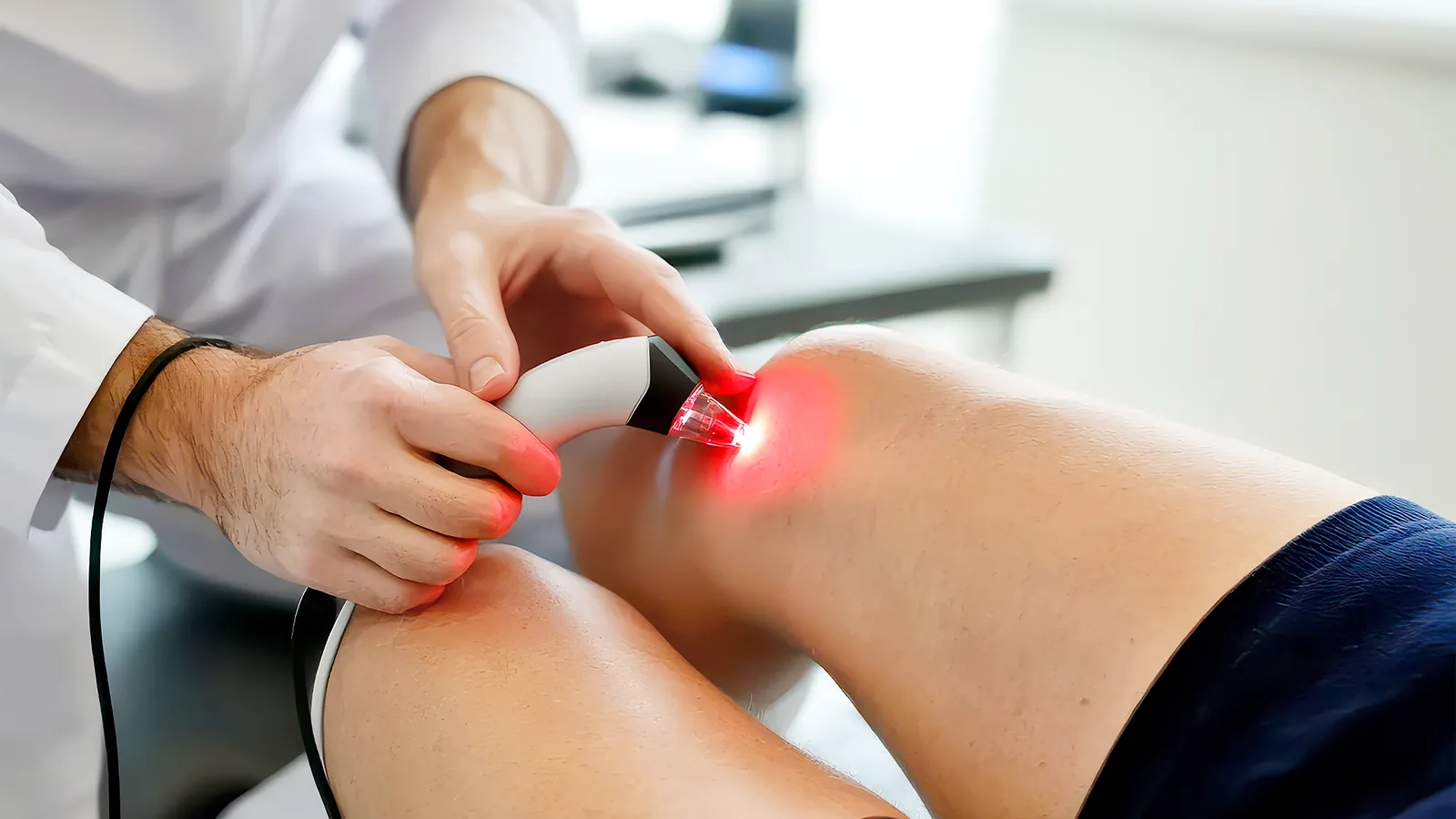 Clinician applying a handheld energy device to a joint, the treated point glowing red